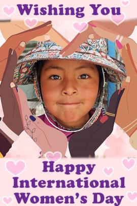 A graphic design of eight human hands arranged in a circle, palms facing the center. Each hand is a different skin tone, representing the races of the world. In the middle of the circle, there is a photo of a little girl's face with shining eyes. She is young and from a South East Asian country. Above and below her appears the title in purple block lettering, appears saying, "Wishing You Happy International Women's Day