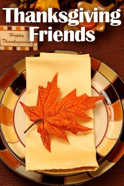 A place setting made of a plate, with a folded napkin on top of it, and an orange fall leaf on top of that.