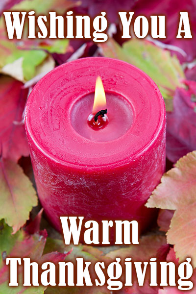 A red candle sitting among an assortment of fallen autumn leaves.