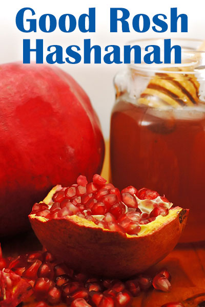 A closeup view of pomegranates. One has been split open to expose its seeds, and there is a pile of seeds on the table in front of it as well.