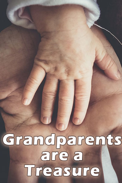 The weathered hand of a grandparent has the smaller hand of a baby resting in its palm.