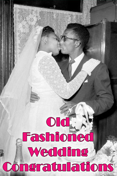 A photo of a young couple circa 1950’s at their wedding reception. The bride in on the left in her wedding gown and white veil; she leans to her groom with a kiss. He is on the right in a dark gray suit and tie and wears glasses. They are kissing each other standing in front of their wedding cake on the table The title of the Wedding greeting card is at the bottom of the image in hot pink letters, "Old Fashioned Wedding Congratulations"