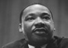 A historical black and white photo of civil rights leader, Martin Luther King Jr. He is speaking, and leaning on a podium.