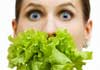 An alarmed-looking woman holding a bundle of lettuce leaves in her mouth.