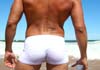 A man stands on a beach with his back to us. He is wearing a very tight pair of white swim trunks that accentuate his muscular butt. The ecard title Sexy Beach Dude Birthday is written in the foreground.