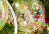 A closeup of a clear glass Christmas ball ornament on a Christmas tree. The lights from the tree reflect on its surface , and there is a little tree drawn on it. Christmas Across The Miles is written below it.