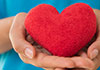 A pair of hands gently cradle a red stuffed heart toy.