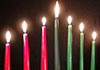 A beautiful carved wood kinara, with seven lit candles. The ecard title Kwanzaa is above.