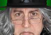A grumpy looking man with long grey hair, a stovepipe hat, and wire framed glasses sitting crookedly on his nose. 30 Second Scrooge is written in the foreground.